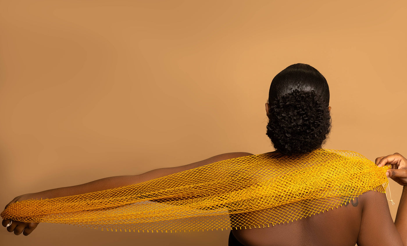 A person holding a yellow traditional African bath sponge, known as the sapo sponge, against a beige background.