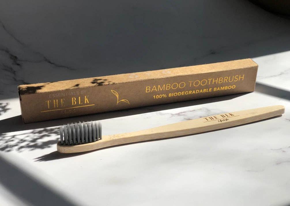 A bamboo charcoal-infused toothbrush with biodegradable bamboo handle and black and white plastic-free nylon bristles, displayed next to its packaging.