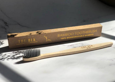 A bamboo charcoal-infused toothbrush with biodegradable bamboo handle and black and white plastic-free nylon bristles, displayed next to its packaging.